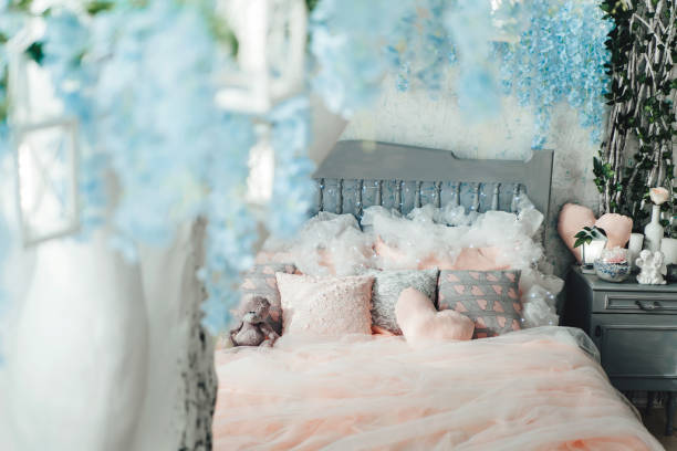 istock Charming bedroom with pastel pink bedding, soft pillows, and teddy bear. View from blurred white tree with blue flowers and lanterns, adding a magical touch. Suitable for home decor, interior design 2156381825