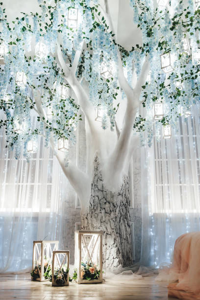 istock Illuminated white tree with blue flowers and hanging lanterns in a beautifully decorated room. Soft lighting and sheer curtains enhance magical serene ambiance. Wooden floor adds rustic charm 2156382678