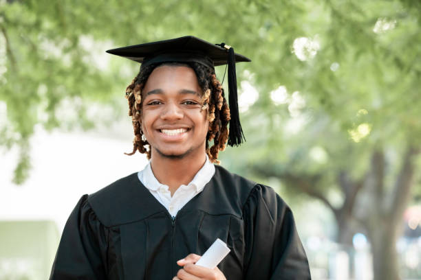 A charming young Black man smiles for the camera at his graduation.