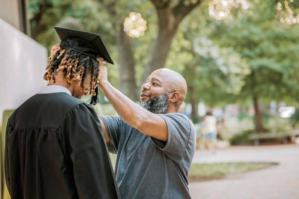 istock As his son prepares for graduation, a dad assists in adjusting his mortarboard cap. 2156394109