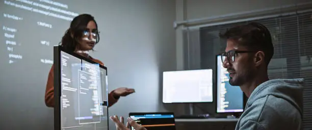 Photo of Hispanic Latin American software engineer developer use laptop computer program coding, projection screen presentation. Programming language development, business technology, night work people concept