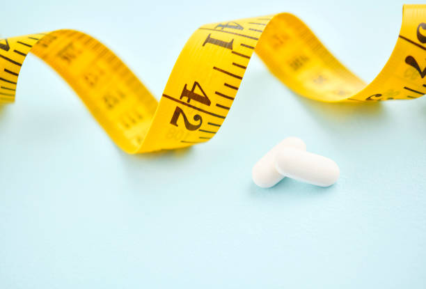 istock Tape measure with diet pills on a blue background 2156400243