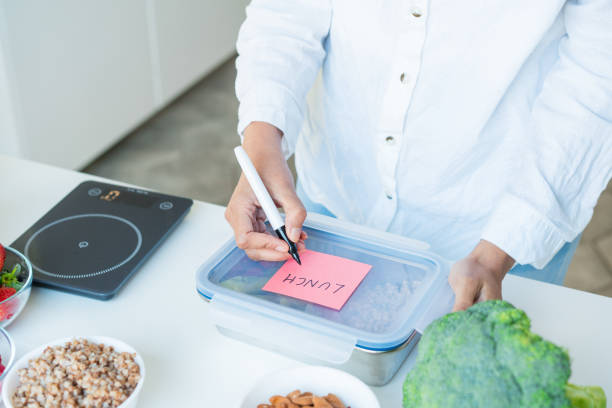 Healthy diet plan for weight loss, daily ready meal menu. Close up woman putting note on lunch box cooked in advance, ready to eat for lunch. Balanced portion with healthy dish. Pre-cooking concept plan de dieta saludable para bajar de peso, menú diario de comidas preparadas. mujer de cerca poniendo nota en la lonchera cocinada de antemano, lista para comer para el almuerzo. porción equilibrada con plato saludable. concepto de precocción.