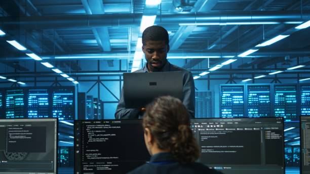 istock Team leader holding laptop supervising employees in server room 2156403667