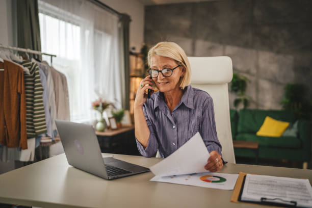 istock Mature woman work from home talk on mobile phone and hold document 2156408639