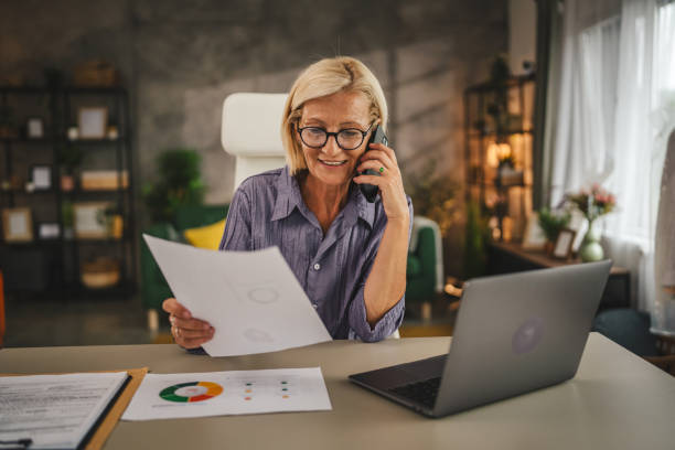 istock Mature woman work from home talk on mobile phone and hold document 2156408672