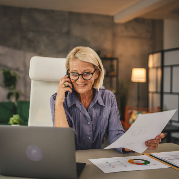 Mature woman work from home talk on mobile phone and hold document