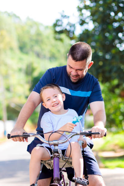 Teenage brother helps his younger sibling learn to ride a bike with training wheels on a sunny summer day. Family bonding, support, childhood development, outdoor fun and learning. Copyspace.