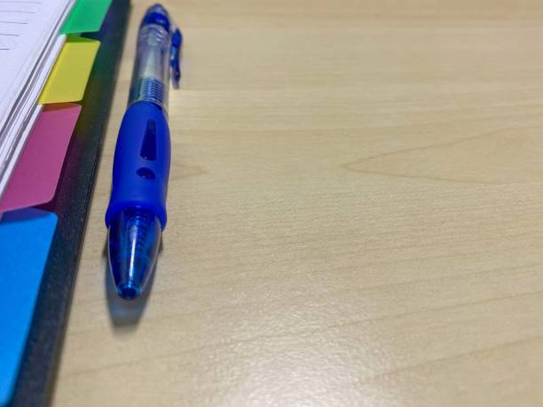 Close-up of notebook and blue pen on wooden table.