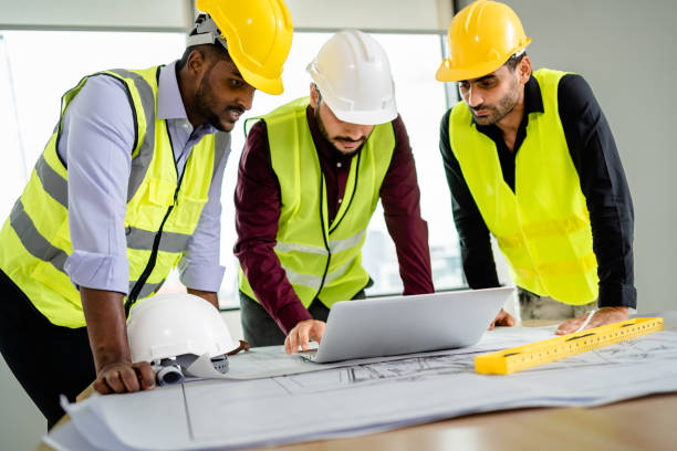 istock Team of Engineers diverse in safety suite discussing architectural projects with blueprints and laptop on the desk at the workplace, Developer real estate, teamwork, architecture, construction concept 2156420289