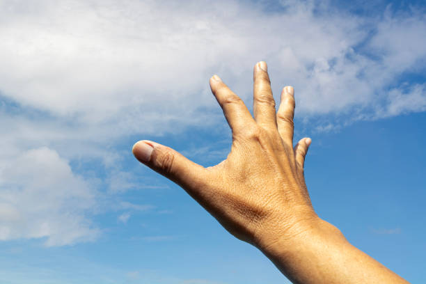 One right hand reached up to the bright blue sky and white cloud whishing for help or something on heaven.