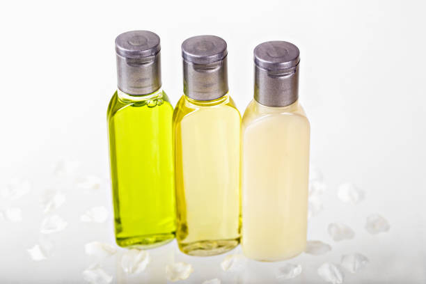 Mockup. Three transparent bottles with different colored cosmetic oils on white surface with scattered petals. Shampoo, shower gel, body lotion. Travels, tourism, hotels. Natural organic cosmetics