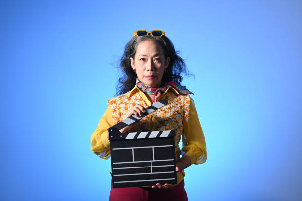 middle age woman holding clapperboard isolated on blue background