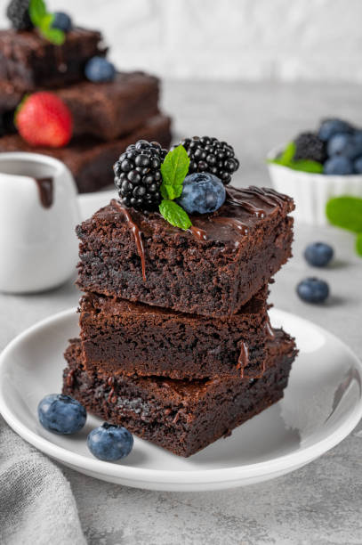 istock A stack of chocolate brownies with chocolate glaze, fresh berries and mint leaves on top on a white plate on a gray concrete background. Delicious dessert. 2156456847