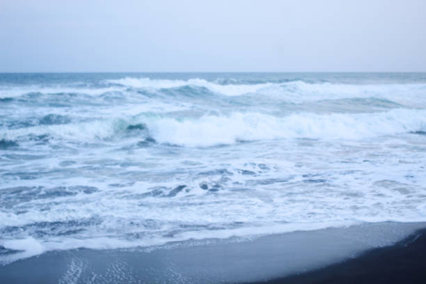 As the tide sweeps in at South Jogja Jetis Beach, Cornwall under a serene sky, waves gently roll, accompanied by ripples and bubbling foam.