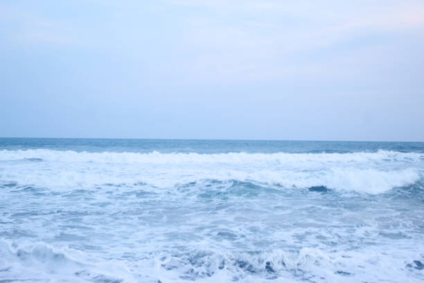 As the tide sweeps in at South Jogja Jetis Beach, Cornwall under a serene sky, waves gently roll, accompanied by ripples and bubbling foam.