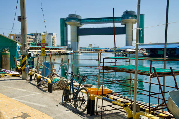 Samcheok City, South Korea - May 18, 2024: A bicycle parked in the foreground with the Tsunami Safety Tower visible at the entrance of Samcheok Port, highlighting both the local transportation and maritime infrastructure.