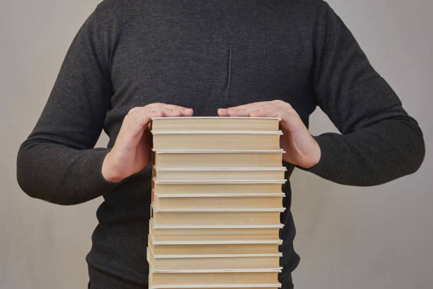 istock Student's hands are on top of a large stack of books. High academic workload at school, large amount of data, numerous tasks for study and completion, library books for students 2156463766
