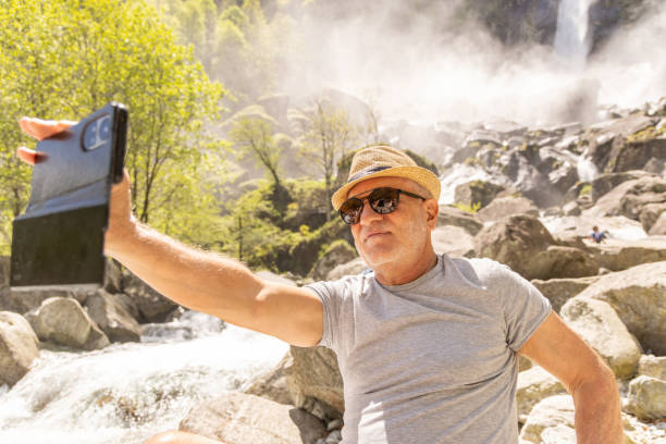 istock Older Man Taking Selfie Near Rocky Waterfall 2156465519