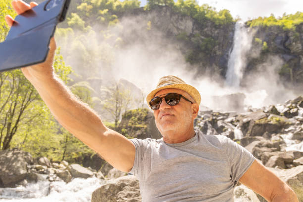 istock Senior Man Taking Selfie Near Rocky Waterfall 2156465522
