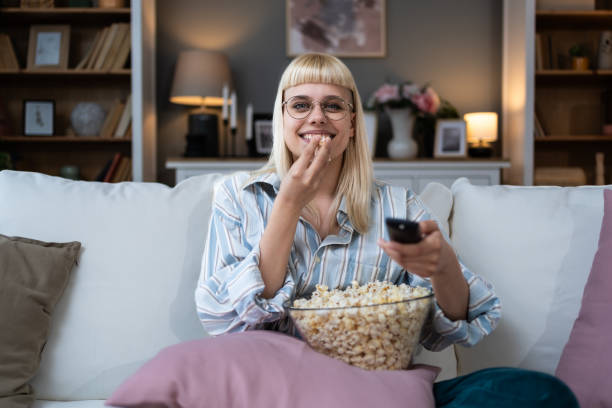 istock Young happy freshly divorced or recently single woman after toxic relationship breakup sitting alone at home on sofa, eating popcorn and watching movie or television in her new apartment she rented. 2156468575