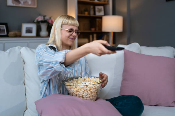 istock Young happy freshly divorced or recently single woman after toxic relationship breakup sitting alone at home on sofa, eating popcorn and watching movie or television in her new apartment she rented. 2156468598