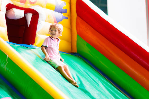 Child jumping on colorful playground trampoline. Kids jump in inflatable bounce castle on kindergarten birthday party Activity and play center for young child. Little boy playing outdoors in summer.