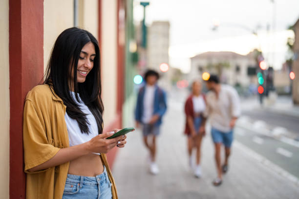 istock Smiling Hispanic Woman Texting on Phone While Waiting Outdoors 2156477335