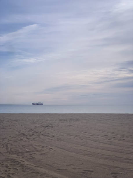 Distant view of a large ship in sea. Empty beach with nautical vessel far in ocean on overcast sky.