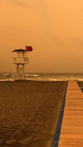 White lifeguard tower stands on a sandy beach with boardwalk overlooking sea during sunset.  A wooden walkway leads up to the beach.