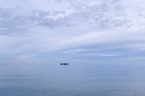 Calm sea surface extending towards the horizon with large nautical vessel under cloudy sky.  Natural splendor of the seascape.