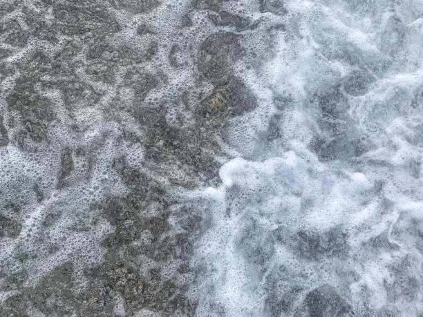 White foam from the sea waves and pebbles on the shore. Waves create foam over pebbles on the beach.