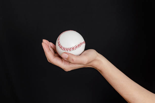istock Hand holding a baseball on black background. Baseball game concept 2156482612