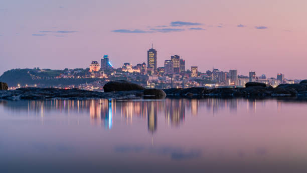 Pink sky over old Quebec city skyline at dusk, as the street lights light up, with its reflection at low tide. QC, Canada