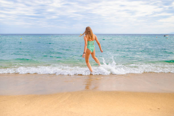 Rear-view of unrecognizable young Caucasian woman playing with waves on the beach
