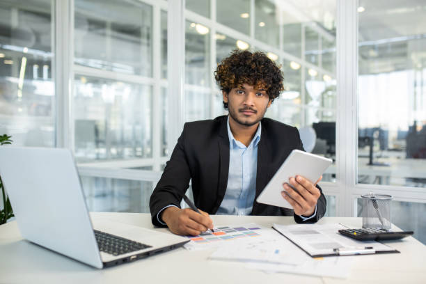 istock Young businessman working on tablet in modern office with laptop and documents 2156500894