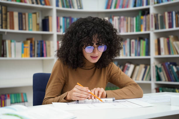 istock Wavy haired woman interior design student working on diploma project in university library 2156501603