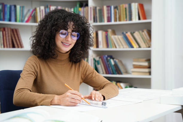 istock Smiling woman architect working with blueprints in a well-stocked library 2156501629