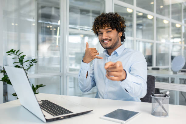 istock Cheerful businessman making call me gesture and pointing at camera in modern office setting 2156504062