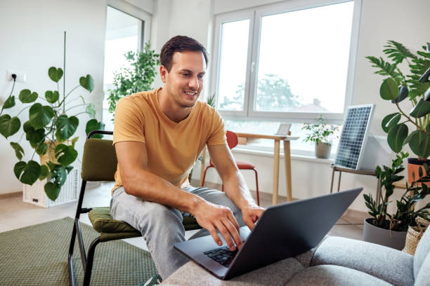 istock Young casually clothed smiling man using laptop while relaxing at home 2156505620