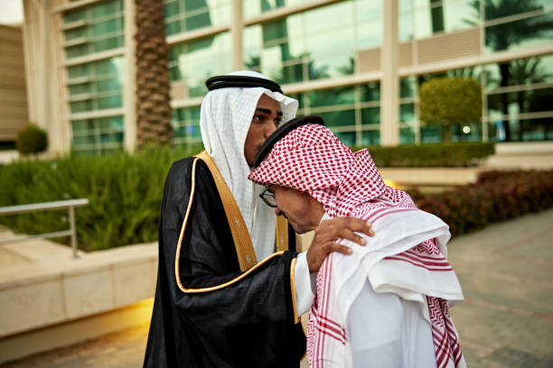 Saudi boy kissing on man's head wearing thawb while standing in university campus