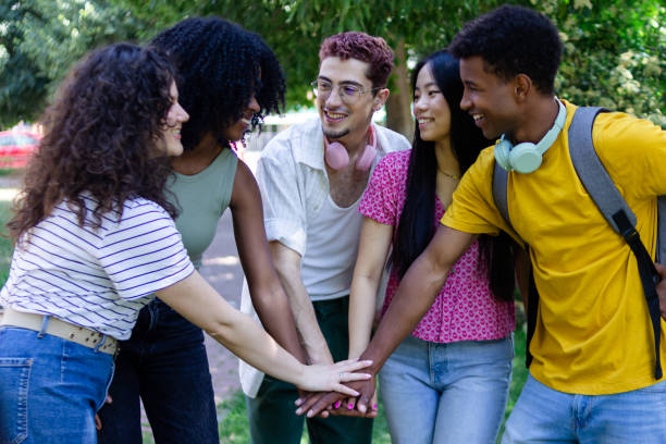 istock Group of five happy and diverse students putting hands together in a park 2156510507