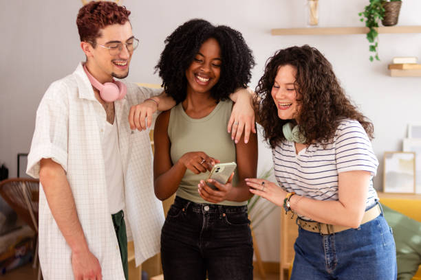 istock Three diverse friends laughing and having fun using smartphone indoors 2156511121