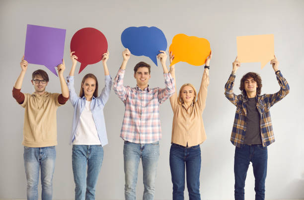 istock Happy young people holding clean speech bubbles standing on gray studio background 2156513434