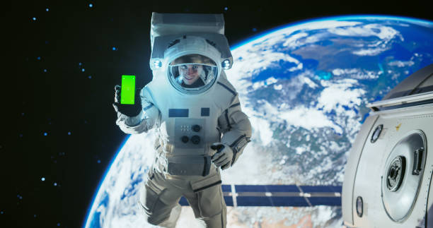 istock Young Astronaut Floating in Space in Zero Gravity. Spaceman Showing a Smartphone with Green Screen Mock-Up Template. Male in a Spacesuit Posing for Camera, Smiling in Open Space Outside a Spacecraft 2156518381