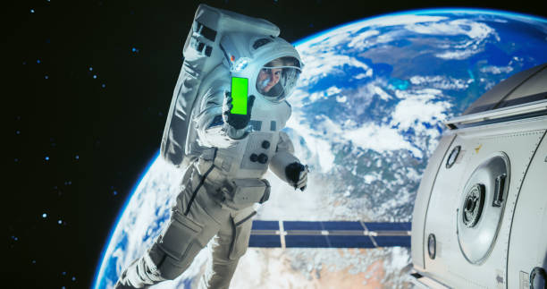 istock Young Astronaut Floating in Space in Zero Gravity. Spaceman Showing a Smartphone with Green Screen Mock Up Template. Male in a Spacesuit Posing for Camera, Smiling in Open Space Outside a Spacecraft 2156518420