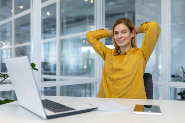 istock Smiling woman relaxing at office desk with laptop and notepad 2156518511
