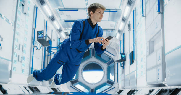 istock Male Astronaut Floating in Zero Gravity Inside a Space Station. Spaceman Using Smartphone in Space in Orbiting Spacecraft, Browsing Internet Content and Checking and Updating Social Media Networks. 2156519761
