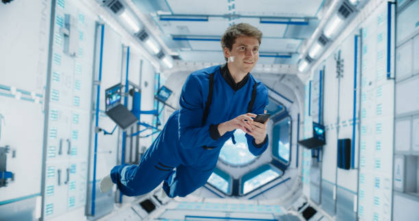 istock Male Astronaut Floating in Zero Gravity Inside a Space Station. Spaceman Using a Smartphone in Space in Orbiting Spacecraft, Browsing Internet Content and checking and Updating Social Media Networks. 2156519784