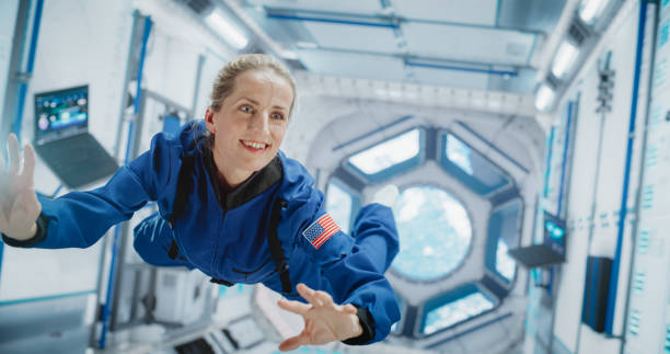 Female Astronaut in Blue Spacesuit Floating Inside the International Space Station, Smiling. Demonstrates Human Achievement in Space Exploration. Cosmos Inspires Scientific Discovery Female Astronaut in Blue Spacesuit Floating Inside the International Space Station, Smiling. Demonstrates Human Achievement in Space Exploration. Cosmos Inspires Scientific Discovery space station stock pictures, royalty-free photos & images